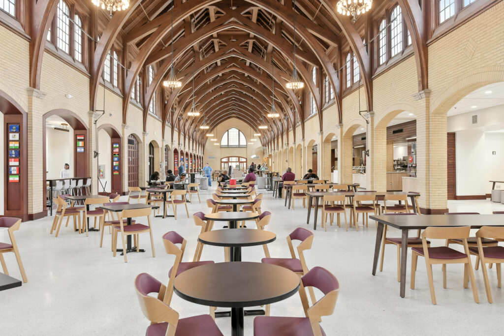 Large dining hall with high vaulted wooden ceilings, yellow brick walls, and many tables and chairs.