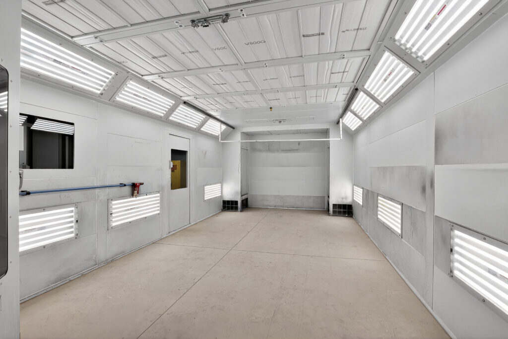 An empty industrial spray paint booth with white walls and overhead LED lighting panels.