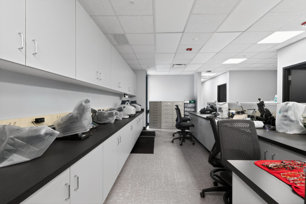 A laboratory workspace with white cabinets, dark countertops, and chairs, featuring various scientific instruments covered in plastic.