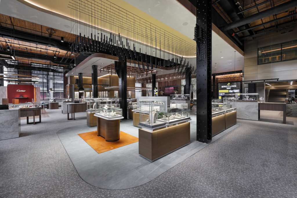 Interior of a luxury jewelry store featuring glass display cases, wood-paneled fixtures, and signage for Cartier and Breitling.