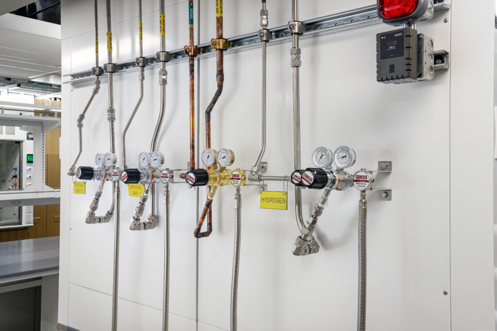 A wall-mounted gas distribution manifold with multiple pipes, pressure regulators, and gauges, including a label for hydrogen.