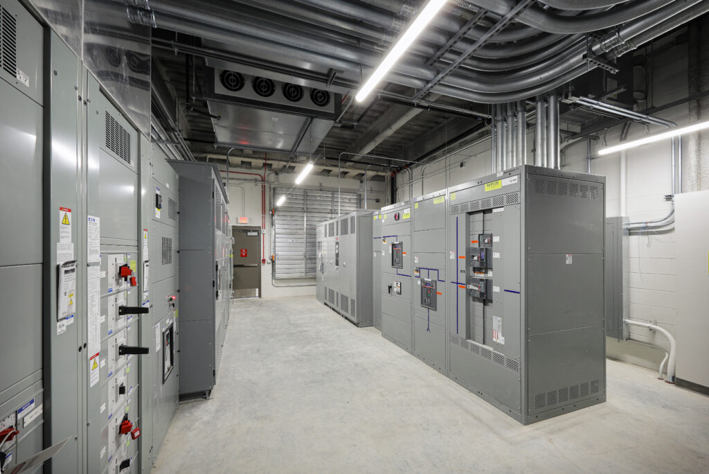Rows of large grey electrical switchgear cabinets in an industrial mechanical room.