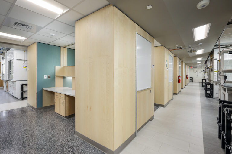 A laboratory corridor featuring light wood-paneled walls, a built-in desk, and a whiteboard.