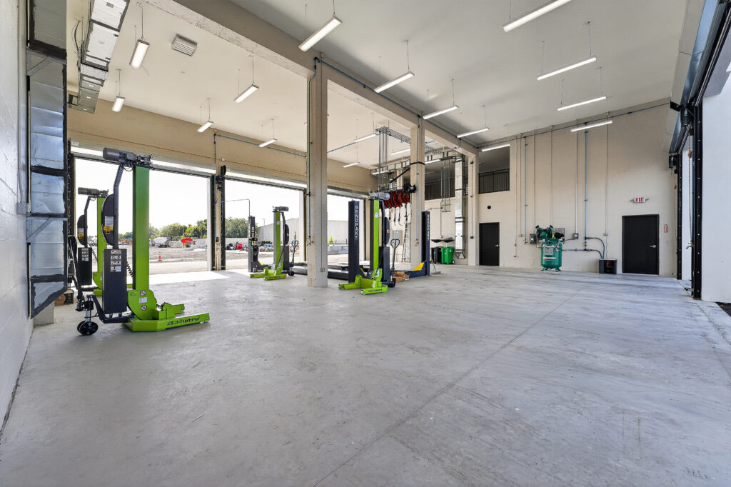 Interior of a spacious automotive garage with three sets of green mobile vehicle lifts in an open-bay workspace.