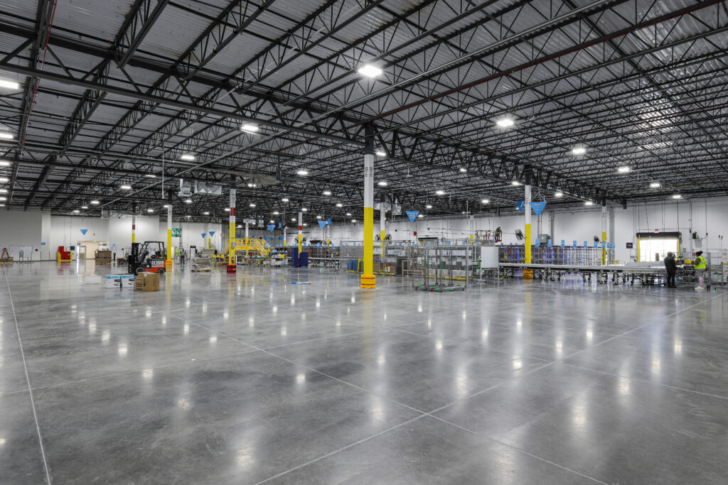 An expansive, high-ceilinged warehouse with a polished concrete floor, rows of industrial equipment, and support columns painted yellow.