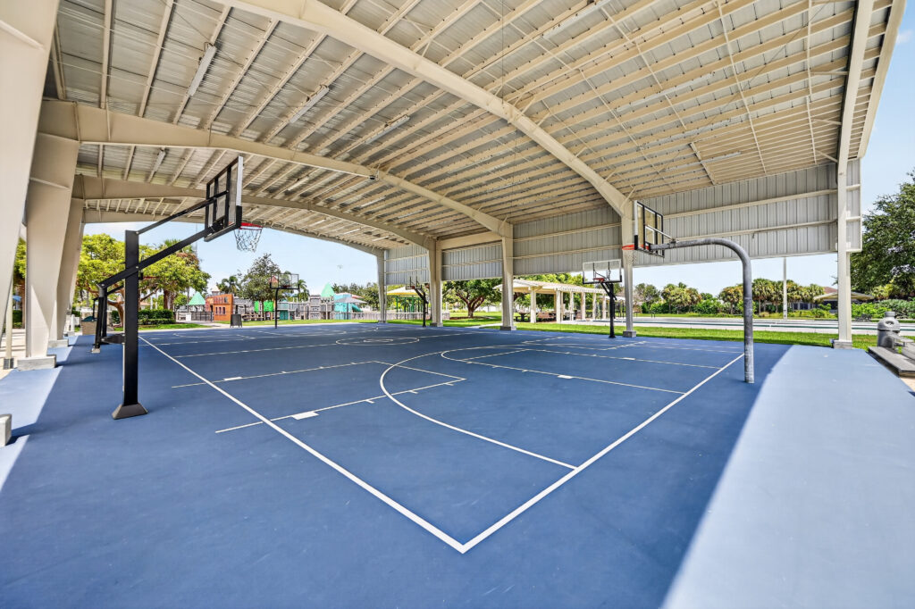 Outdoor basketball court with a blue surface under a large metal pavilion roof.
