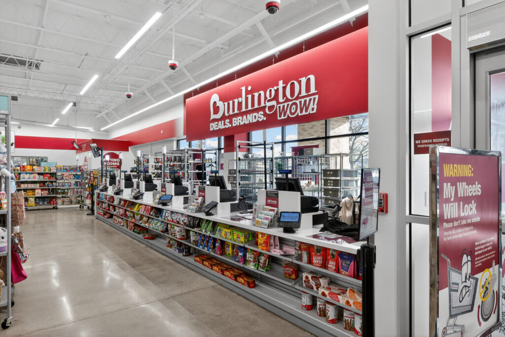 Checkout counters at a Burlington store with shelves of snack items and a warning sign about locking cart wheels.