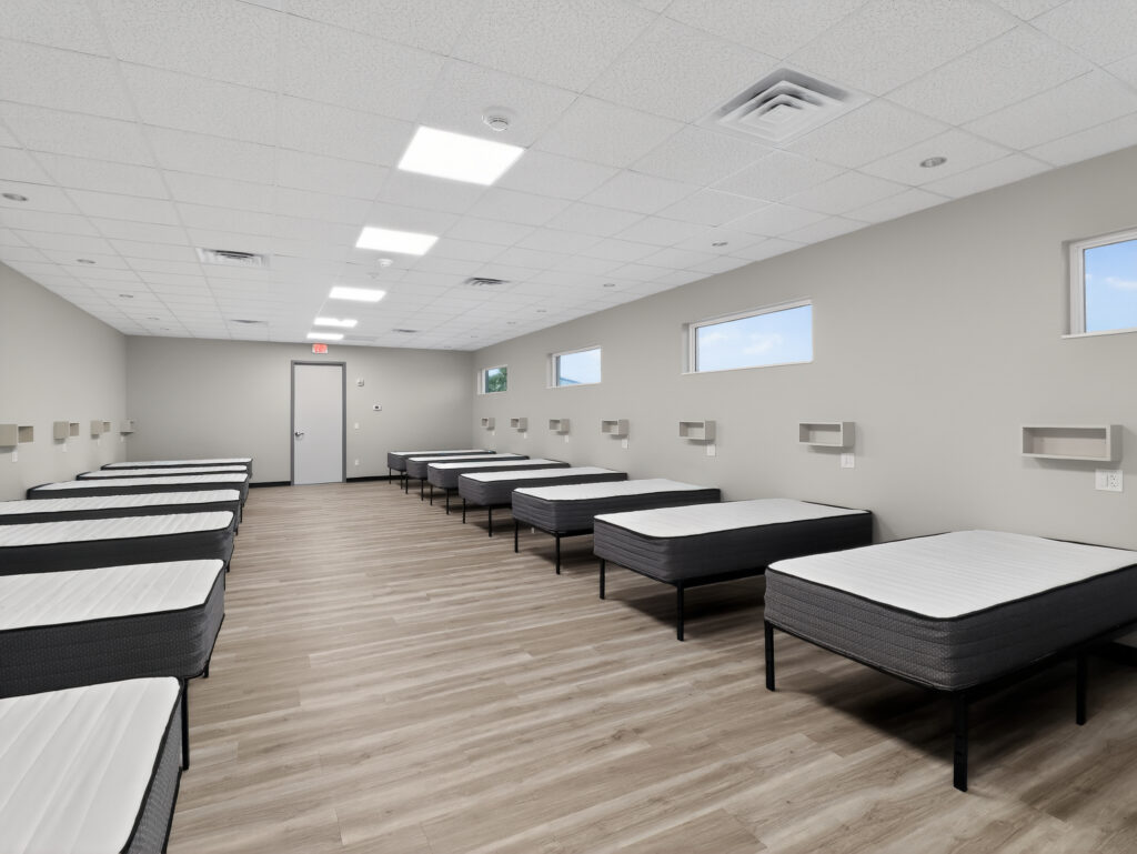 A large room with rows of twin-sized beds and wall-mounted shelves.