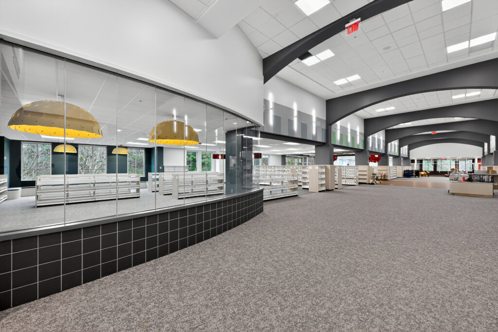 Spacious library interior featuring a glass-enclosed area, tall bookshelves, and large gold pendant lights.