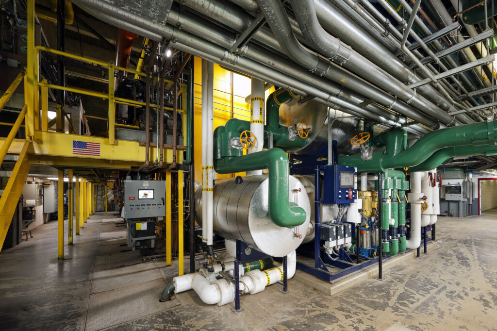 Industrial facility with large pipes, valves, and a control panel, featuring a yellow support structure and a small American flag.