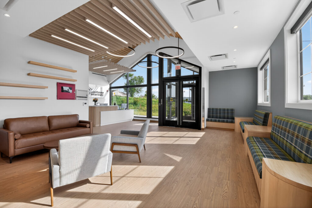 Waiting area of Lakehouse Veterinary with a brown leather sofa, two light grey armchairs, plaid bench seating, and a reception desk in the background.