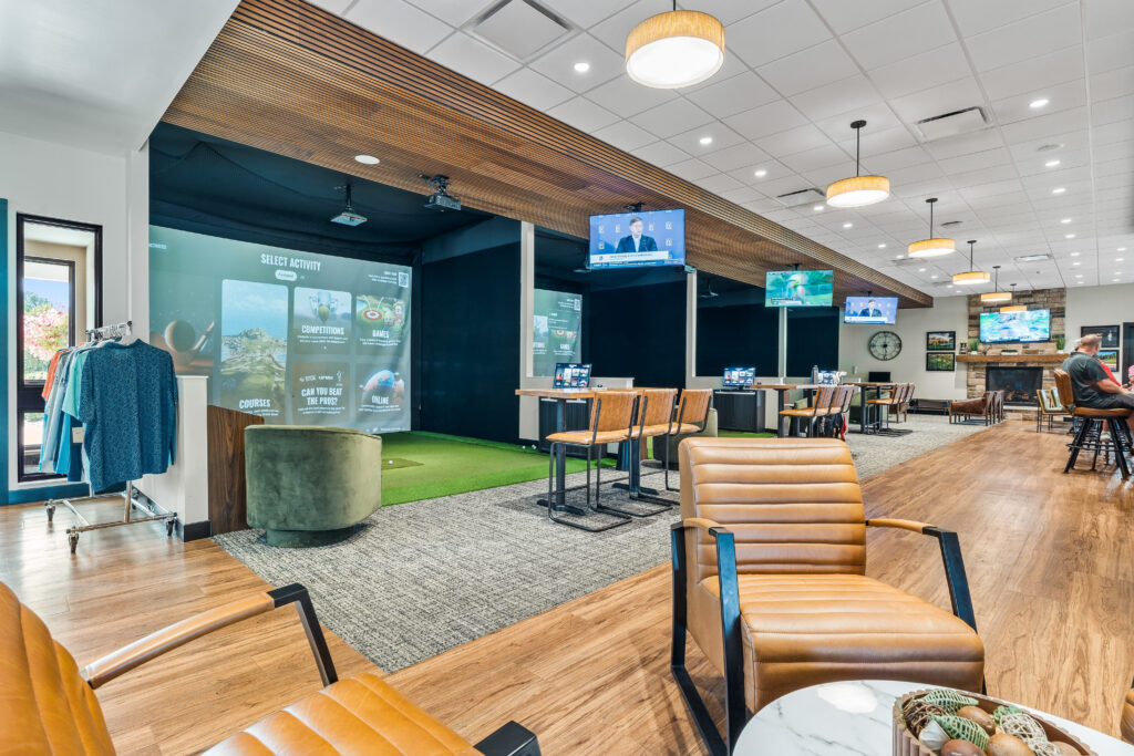 Indoor golf lounge featuring golf simulator bays with touchscreens, seating areas, and a fireplace.