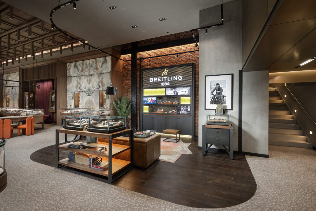 Interior of a Breitling boutique featuring glass display cases, a leather sofa, and a wall-mounted display with the Breitling 1884 logo.