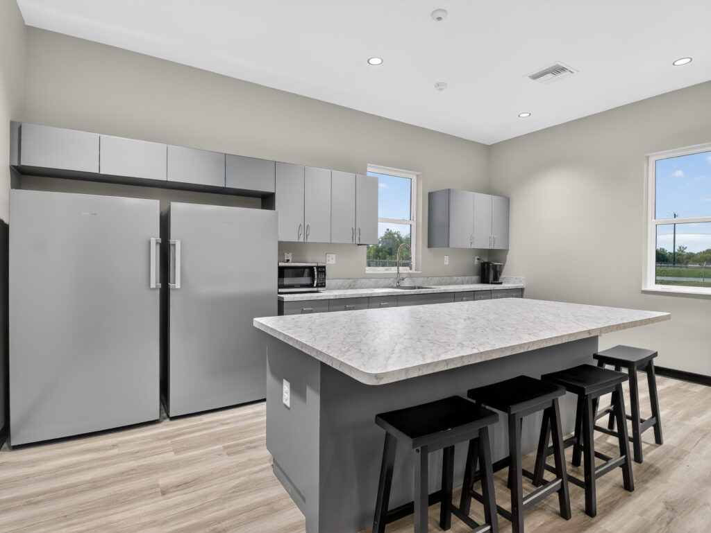 Modern kitchen with gray cabinets, a marble-patterned island with three black stools, and stainless steel appliances.