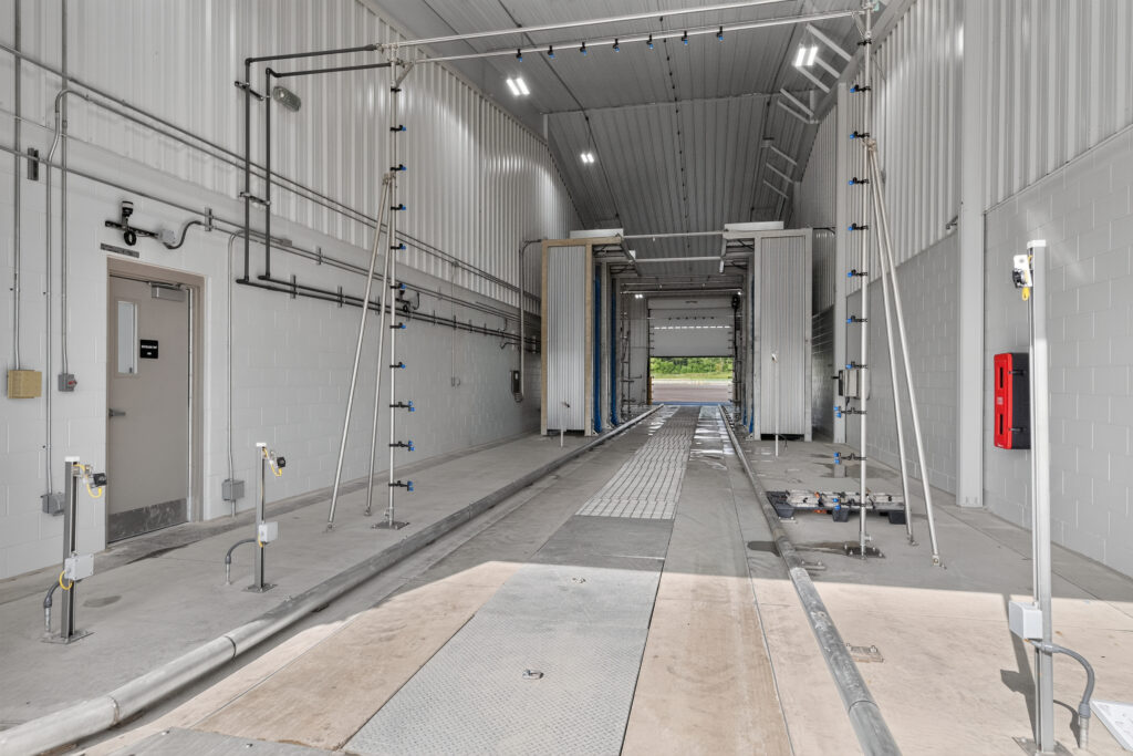 Interior of an automatic vehicle wash bay with overhead spray nozzles and floor tracks.