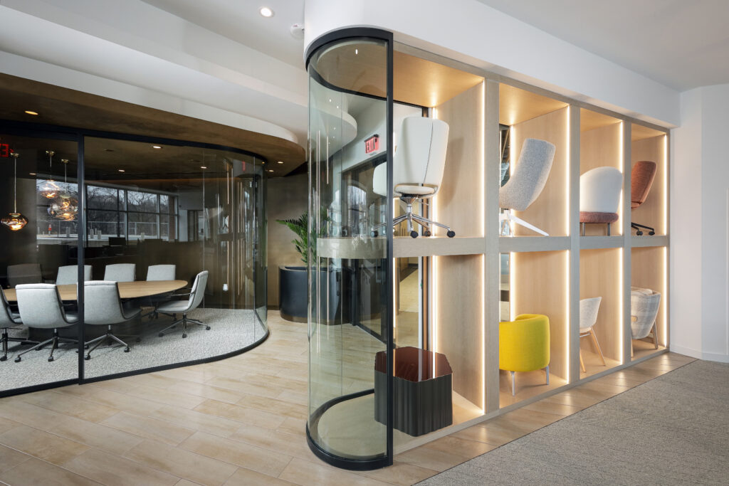 Office interior featuring a glass-enclosed conference room and a shelving unit displaying various office chairs.