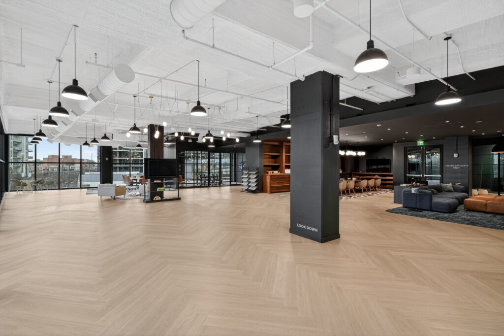 Open-plan office interior with light wood flooring, a central black pillar, and various seating areas.