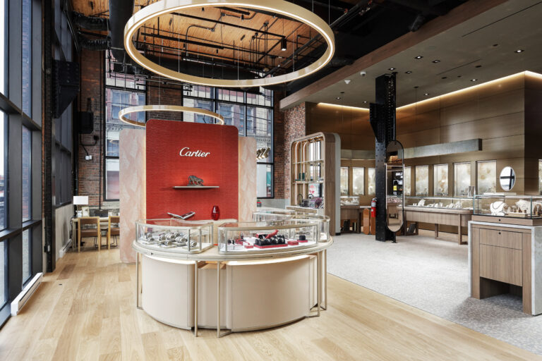 Interior of a Cartier jewelry boutique featuring circular display cases, a branded red wall, and glass jewelry cabinets.