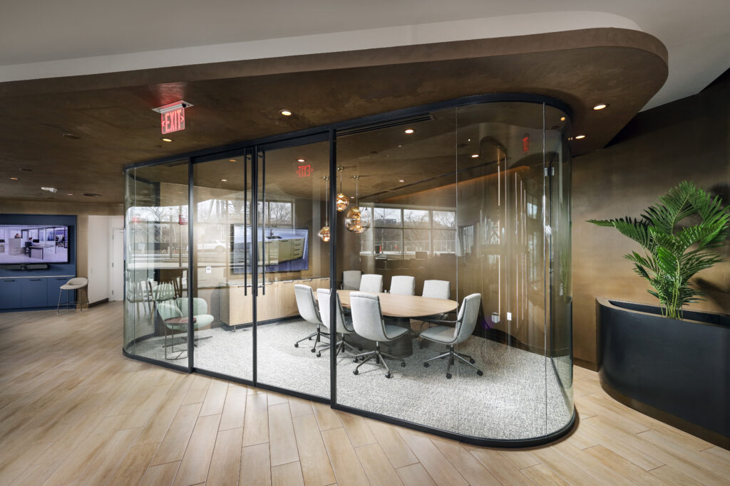 A glass-walled conference room with an oval table and six chairs, situated in an office lobby.