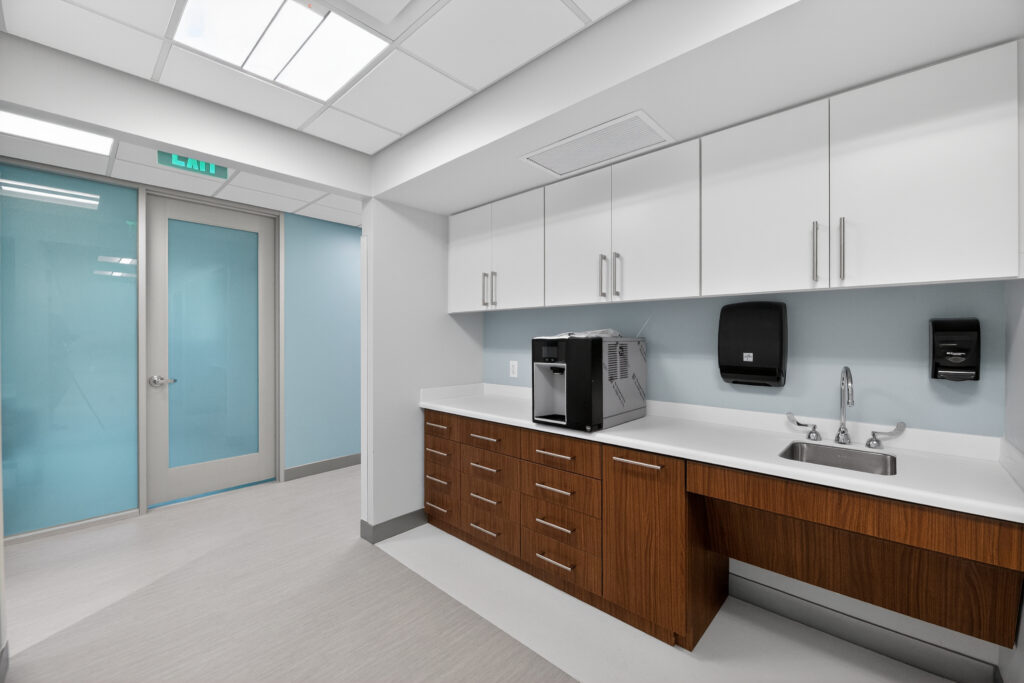 Office break room with white cabinets, wood-tone drawers, a coffee machine, and a sink.