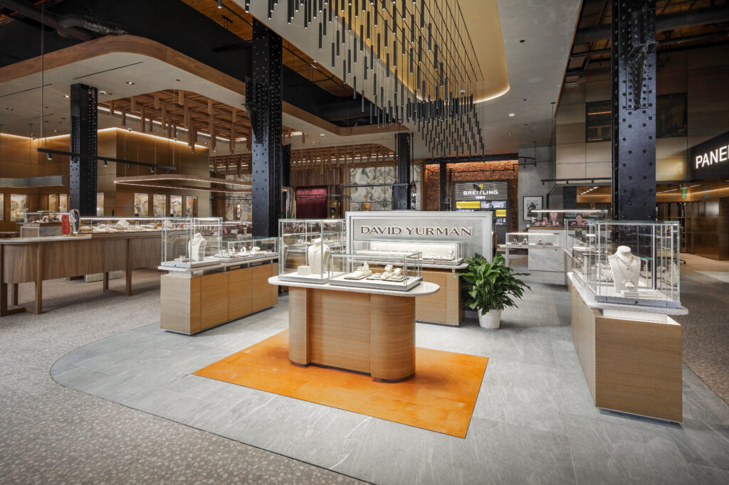 Interior of a jewelry store featuring glass display cases on wooden pedestals, with a prominently placed David Yurman brand sign.