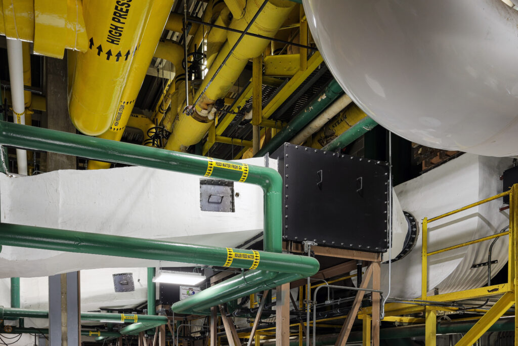 Industrial piping system with yellow high-pressure steam pipes and green feed water pipes running through a plant.