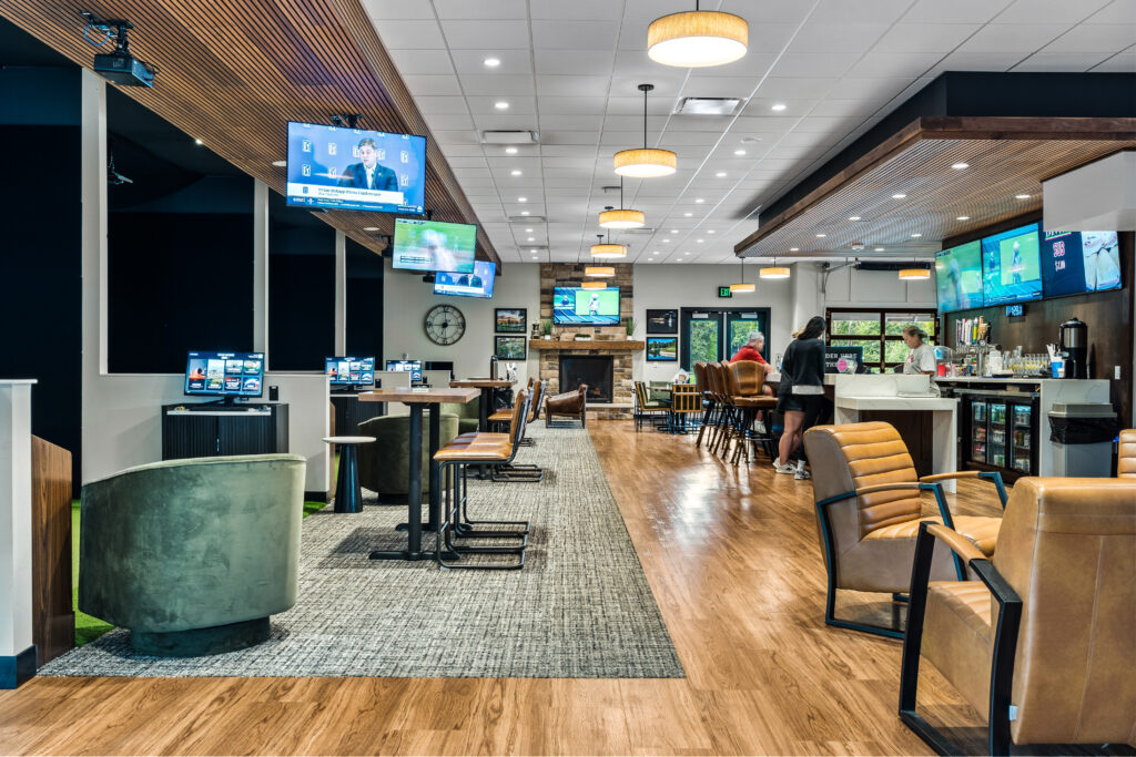 Interior of a restaurant and bar with a fireplace, lounge seating, high-top tables, and televisions mounted on walls.
