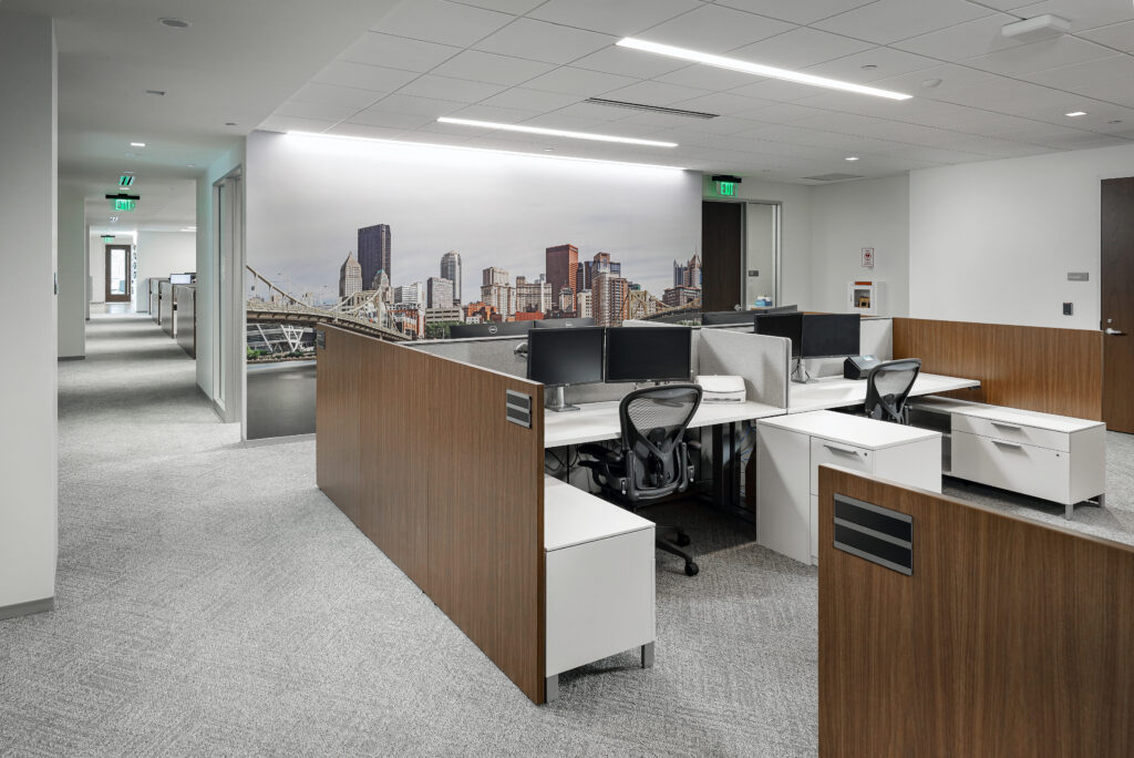 Modern office interior featuring rows of cubicles with wood-paneled walls and a large wall mural of a city skyline.