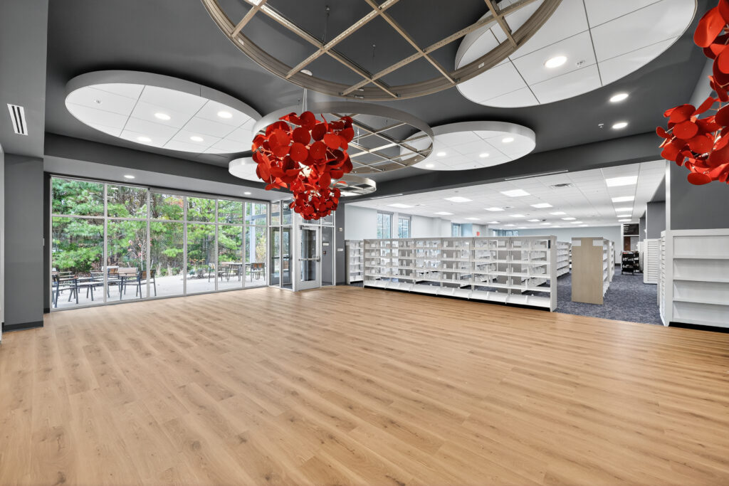 Open library space with light wood flooring, rows of white bookshelves, and large hanging red sculptural light fixtures.