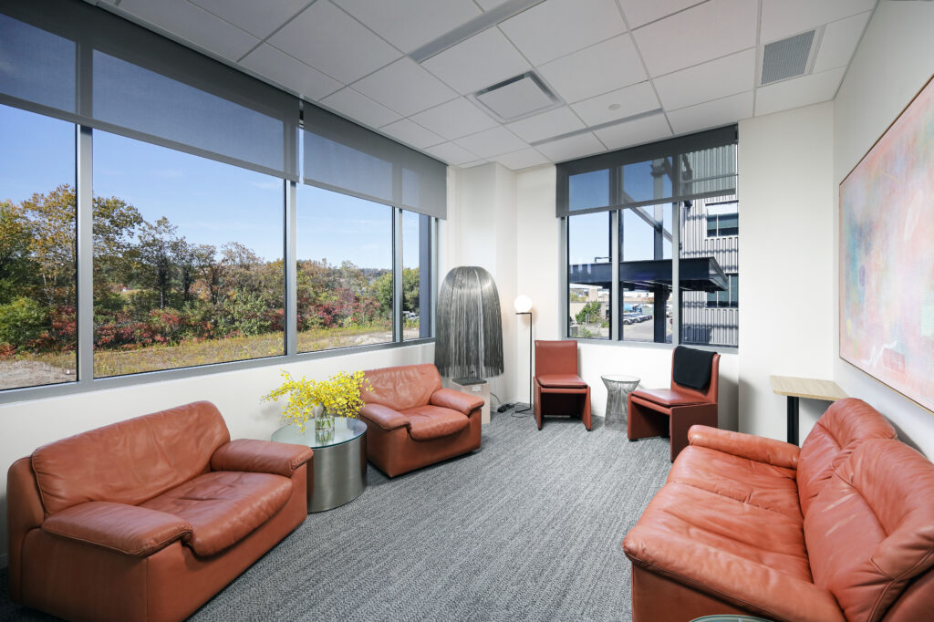 A lounge area with leather seating including two armchairs, a loveseat, and two chairs, arranged around small tables in front of large windows.