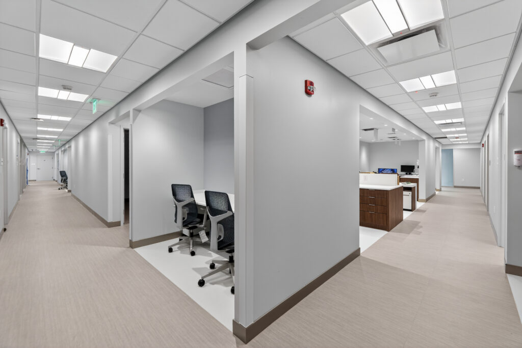 A modern office hallway with a small, private workspace containing two desk chairs.