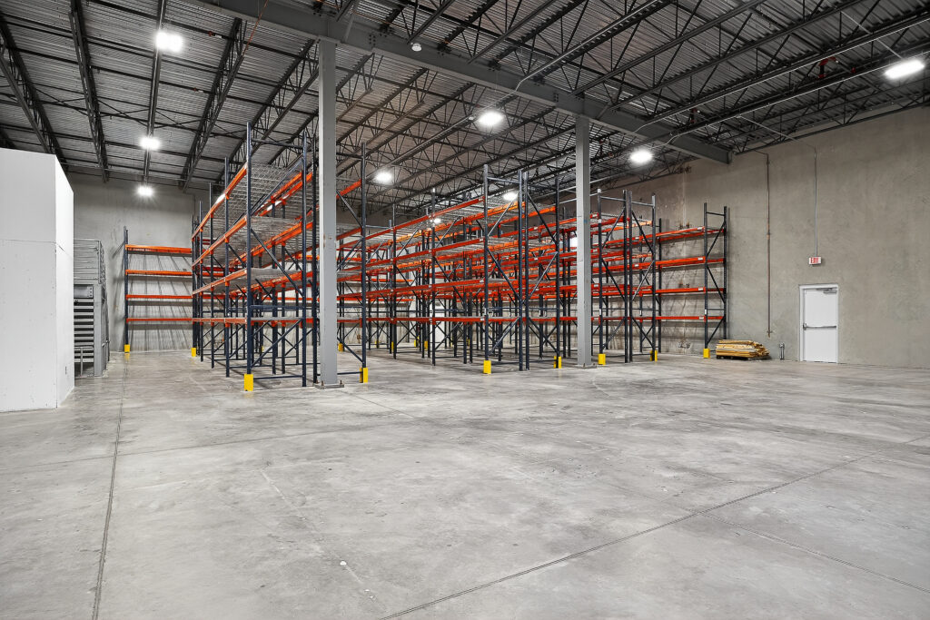 Empty industrial warehouse featuring rows of tall, orange and blue steel pallet racking.