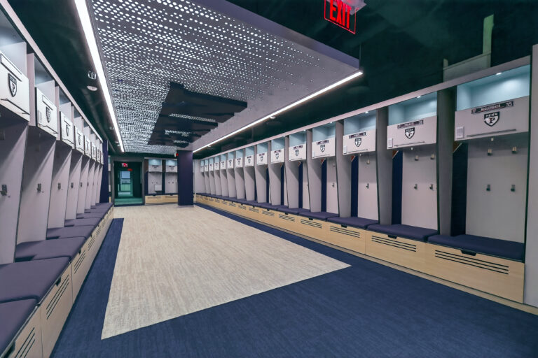 Empty athletic locker room with rows of lockers labeled with the Penn logo and player names.