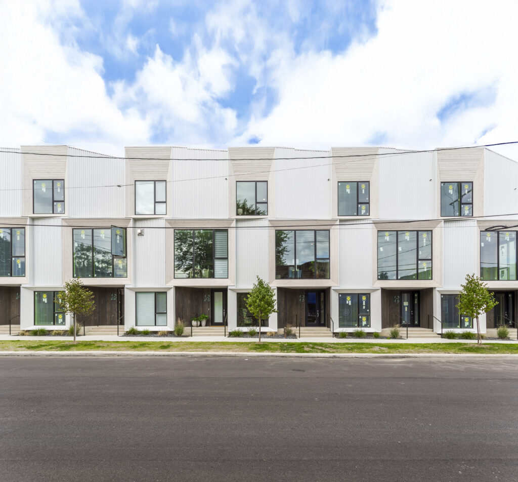 A row of modern townhomes with white metal siding, dark wood entryways, and large windows.