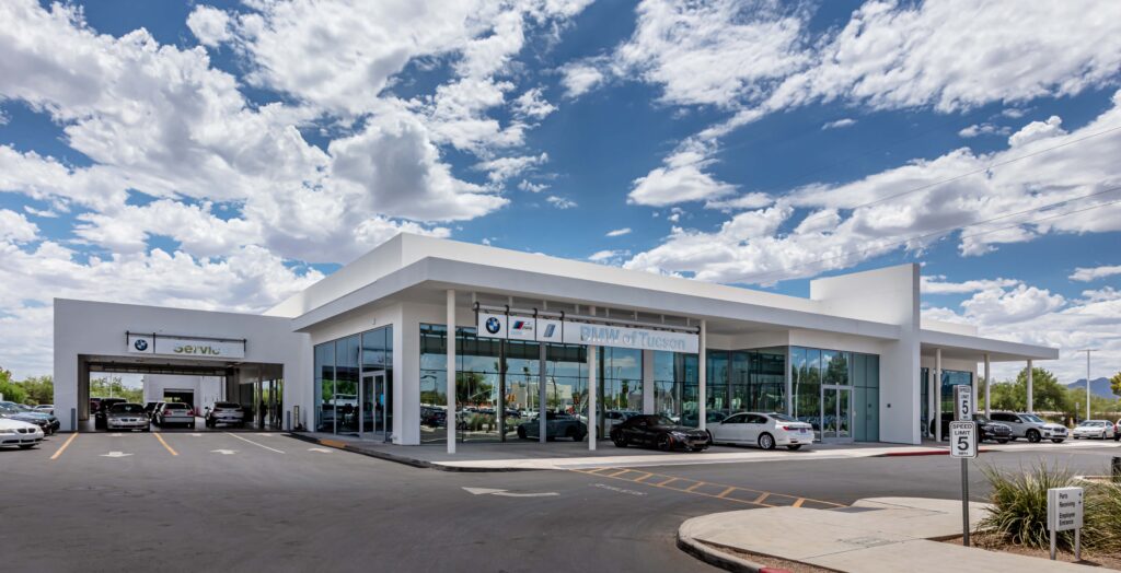 Exterior of the BMW of Tucson dealership building featuring a service bay and glass storefront under a cloudy blue sky.