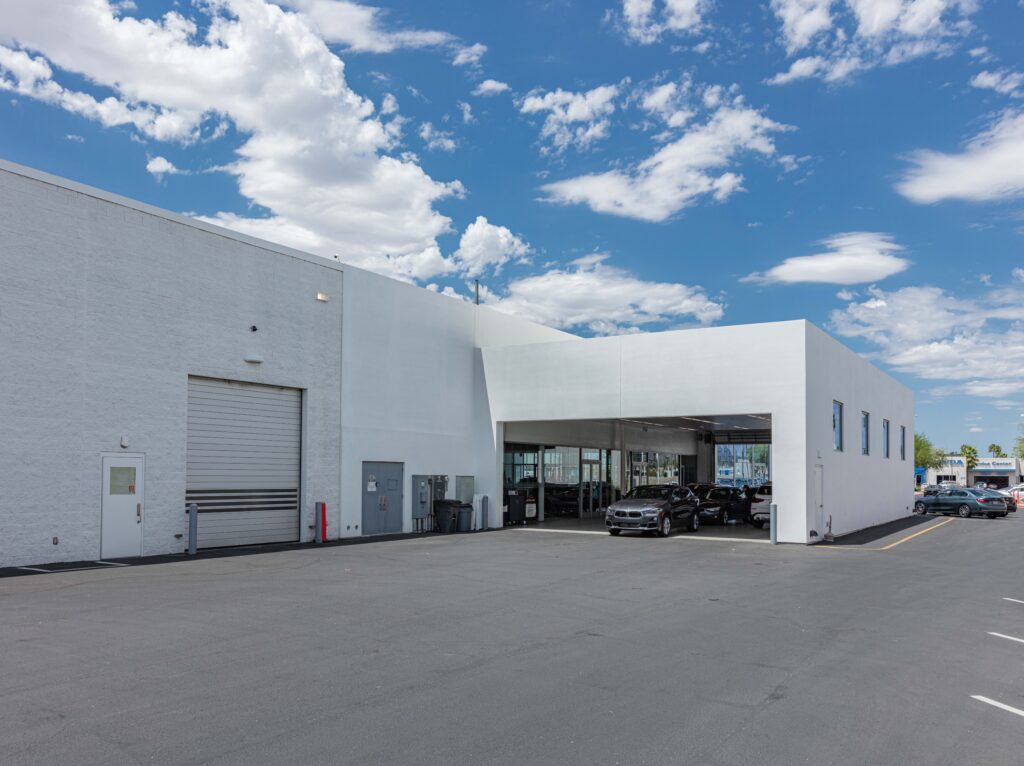 Exterior of a white automotive service building with a large bay entrance and parked cars.