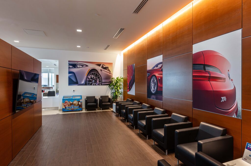 A waiting area with rows of black leather armchairs, wood-paneled walls decorated with BMW car posters, and a Blue Bunny ice cream freezer.