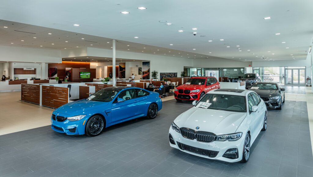 A BMW dealership showroom floor featuring a blue coupe, a white sedan, a red SUV, and a dark grey sedan.