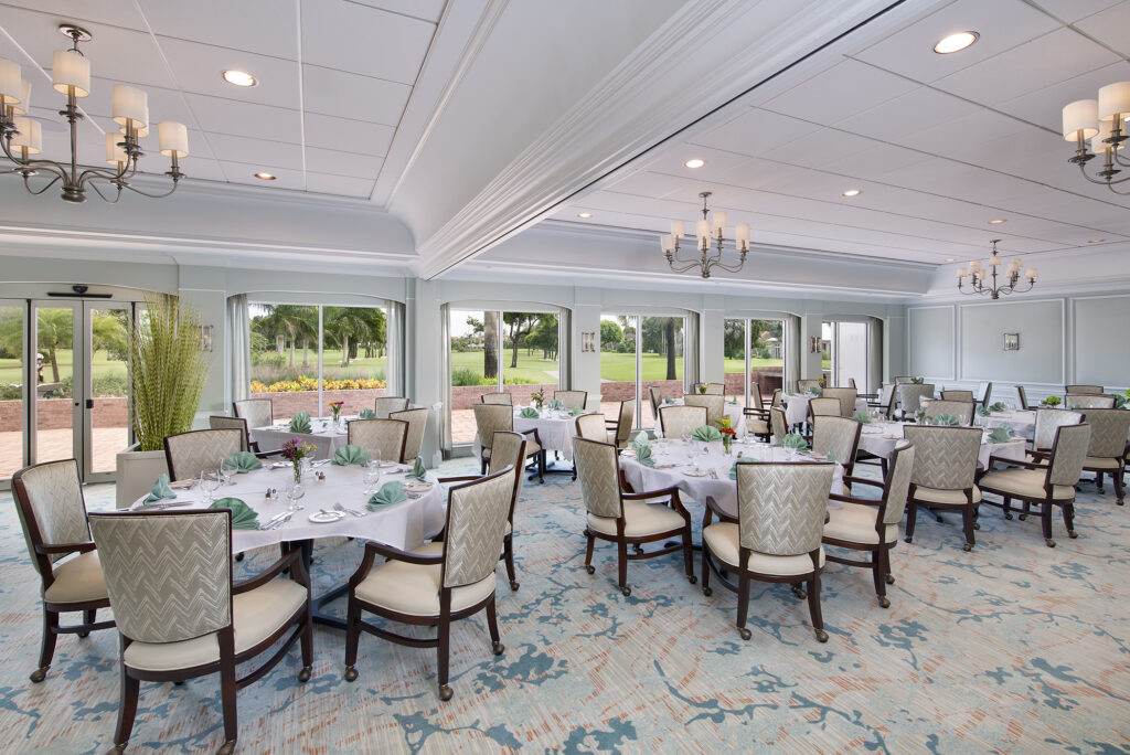 A banquet room with multiple round tables set for dining, overlooking a green golf course through large windows.