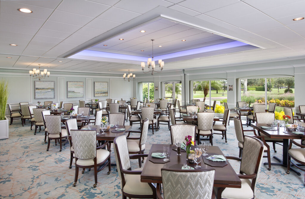 Dining room with many tables, chairs, and large windows overlooking a landscaped garden.