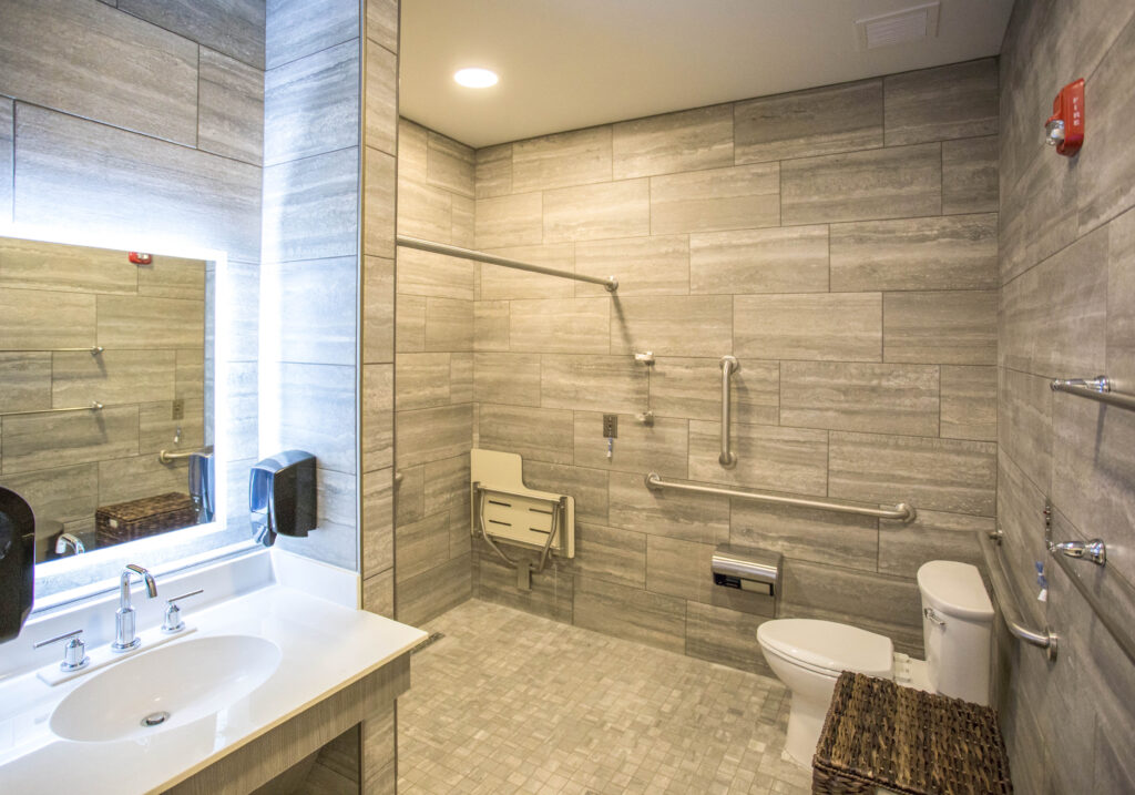 Accessible bathroom with a vanity, toilet, and a walk-in shower featuring a fold-down seat and grab bars.