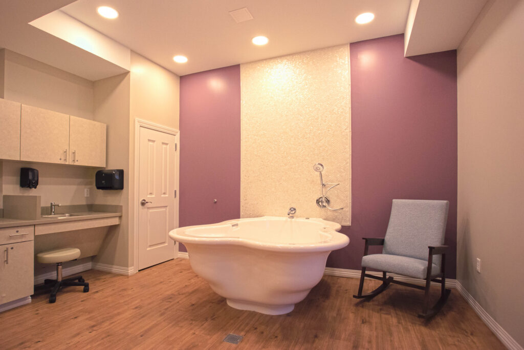 A birth room featuring a large, central soaking tub, a rocking chair, and a cabinet with a small sink.