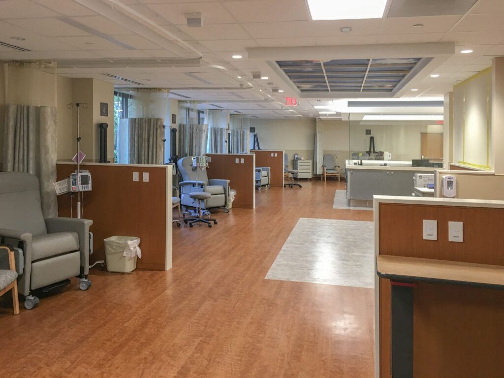 An infusion therapy center with multiple semi-private bays, each containing a medical recliner and IV pole.