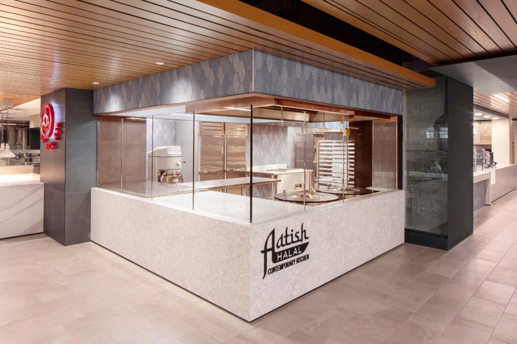 Modern commercial kitchen space with glass walls and a sign that reads, “Adtish Halal Contemporary Kitchen.”