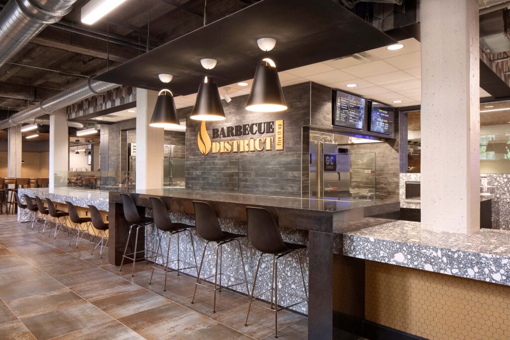 Barbecue District restaurant interior with a stone bar, metal stools, and a black accent wall featuring the restaurant logo.
