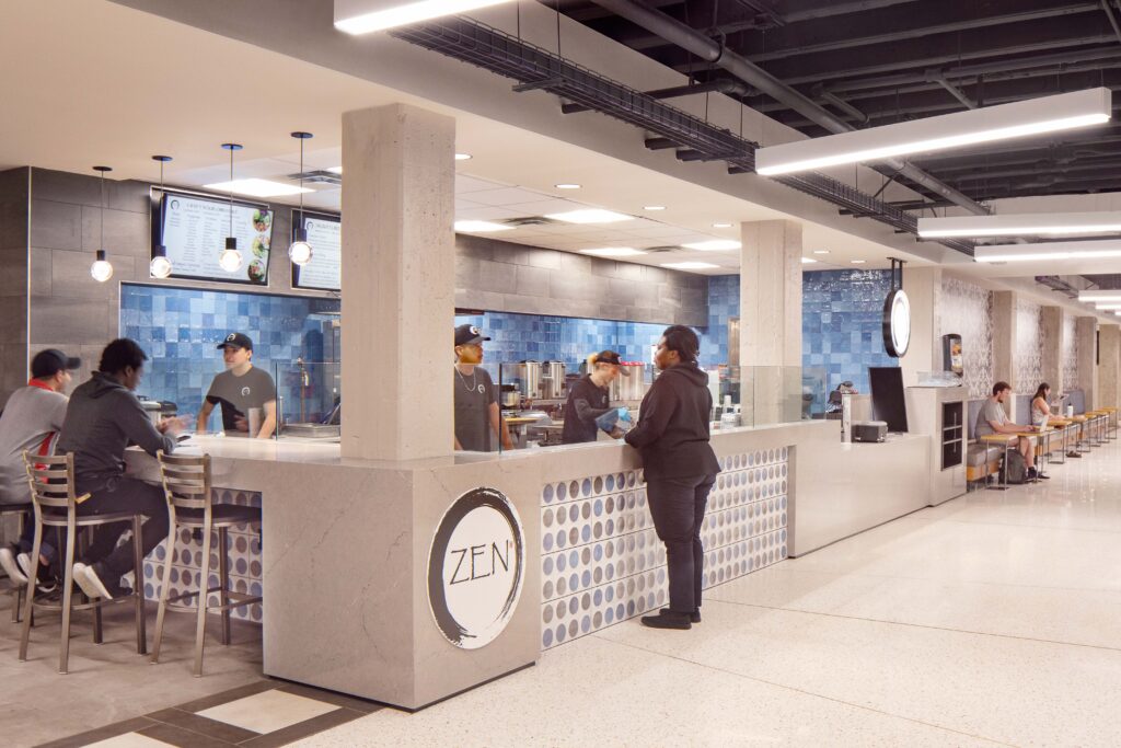 Customers at a Zen restaurant counter ordering food from employees.