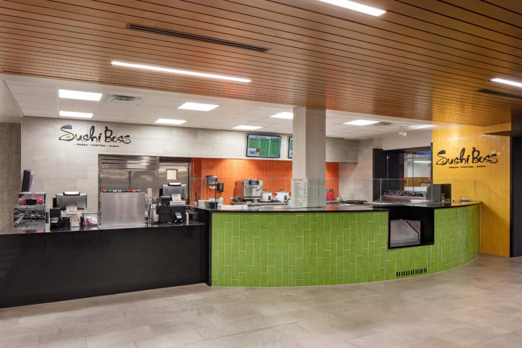 The interior of a Sushi Boss restaurant featuring a curved green tiled service counter, black countertops, and brand signage.