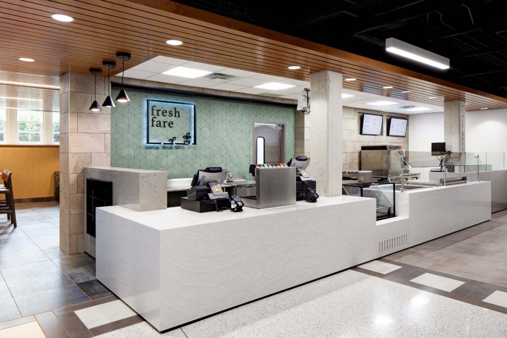 A Fresh Fare service counter with a white stone top, point-of-sale systems, and a green geometric-tiled wall with a logo sign.