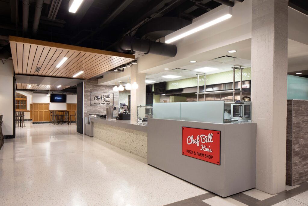 Chef Bill Kim’s Pizza & Parm Shop counter with a red sign in a modern food hall.