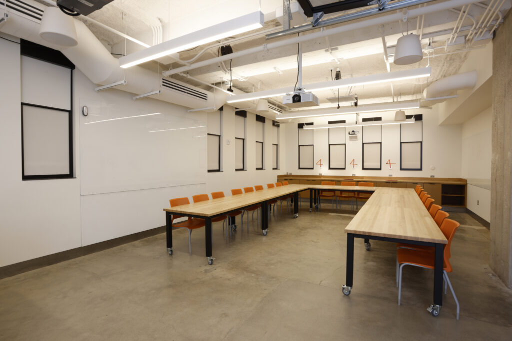 A U-shaped conference table with orange chairs in a modern meeting room featuring a large whiteboard and exposed ceiling fixtures.